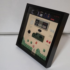 May include: A framed artwork featuring a retro video game theme. The artwork includes a game controller, motherboard, and other components, with text labels like "Connector" and "Body." The background has pixelated graphics and text that reads "Life."