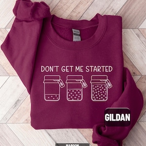 May include: Maroon crewneck sweatshirt with the text "DON'T GET ME STARTED" and three jars with tags. The sweatshirt has a Gildan tag and the word "MAROON" at the bottom. The design is in white.
