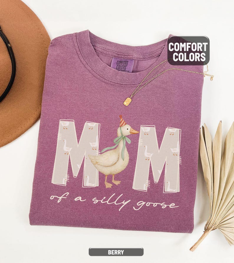 May include: Berry-colored t-shirt with the words "MOM of a silly goose" and a graphic of a goose wearing a party hat and bow. The shirt is made of a soft material and has a crew neck. The Comfort Colors brand tag is visible.