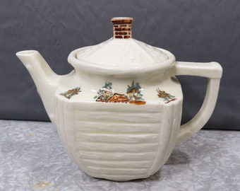 May include: A white ceramic teapot with a brown lid and a brown and green floral design. The teapot has a square body with a ribbed texture and a handle on the side.