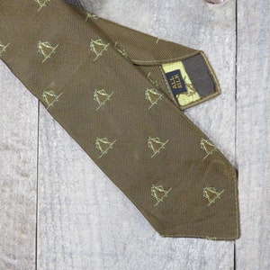 May include: A brown silk tie with a repeating pattern of small yellow figures. The tie has a label that reads "All Silk".