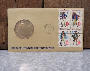 May include: A 1975 Bicentennial First Day Cover envelope with a gold commemorative medal and four 10-cent stamps featuring Continental Army and Navy soldiers. The envelope has a postmark from Washington, D.C. on July 4, 1975.