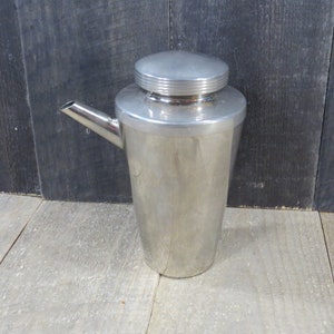 May include: A silver cocktail shaker with a spout and a lid. The shaker is made of metal and has a shiny finish.