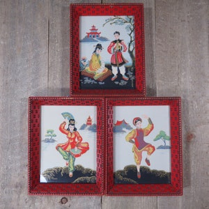 May include: Three framed pictures with red frames and white mats. Each picture depicts a person in traditional Chinese clothing. The pictures are set against a wood background.