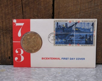 May include: A red, white, and blue first day cover with a gold coin featuring the text "American Revolution Bicentennial" and a depiction of two people. The cover features a stamp with a blue and white illustration of a ship and the text "The Boston Tea Party".