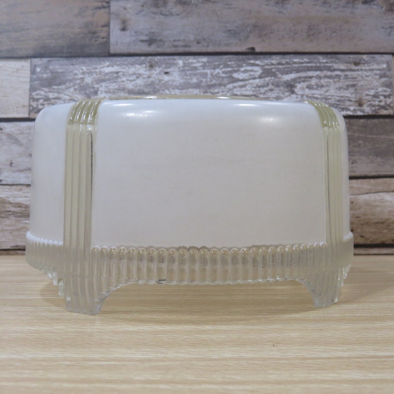 May include: White glass ceiling light fixture with a clear, ribbed design. The fixture has a rounded top and a base with four legs.