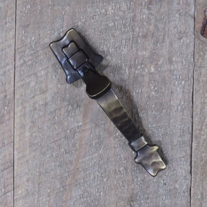 May include: Antique-style brass door handle with a textured finish. The handle has a unique design with a curved shape and a decorative latch.