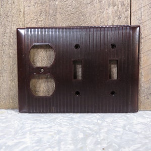 May include: A brown plastic electrical outlet and light switch plate with a ribbed texture. The plate has two toggle switches and a double outlet.