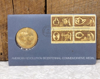 May include: A gold-colored medal with the text "American Revolution Bicentennial Commemorative Medal" on a blue background. The medal is surrounded by four stamps featuring colonial American craftsmen.