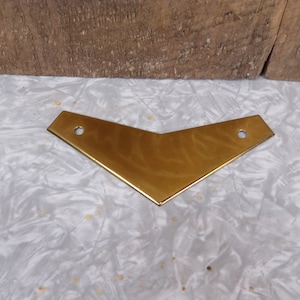 May include: A gold-colored metal bracket in the shape of a chevron. The bracket has two holes on either side.