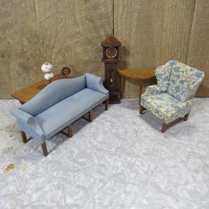 May include: Miniature dollhouse furniture set featuring a light blue sofa, a floral armchair, a wooden grandfather clock, and a small table. The sofa and armchair have wooden legs. The clock has a round clock face.