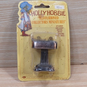 May include: A silver metal pedestal sink with a working faucet, part of the Holly Hobbie "Old Fashioned Collectors Miniatures" series. The packaging features a cartoon illustration of Holly Hobbie.
