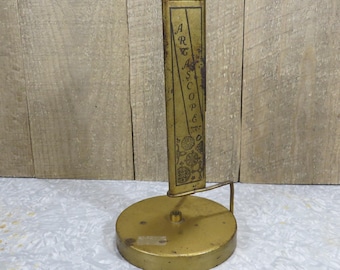 May include: Vintage brass-toned metal Art Scope viewer. The viewer has a round base and a tall, rectangular viewing section with the word "Art Scope" printed vertically. The viewer has decorative floral patterns and is set against a light background.