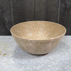 May include: A speckled beige mixing bowl with a wide, rounded shape. The bowl has a speckled pattern of beige, white, and orange. The bowl is made of a durable material and is suitable for kitchen use.
