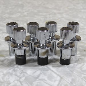 May include: A collection of eight chrome-plated knobs. Each knob features a ridged top, a circular base, and a black rubber or plastic bottom. The knobs are arranged in a group, showcasing their reflective surfaces.