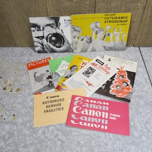 May include: A selection of vintage Canon camera manuals and brochures. The brochures feature images of cameras, people, and text. The colours include black, white, yellow, green, and pink. Some brochures have the Canon logo.