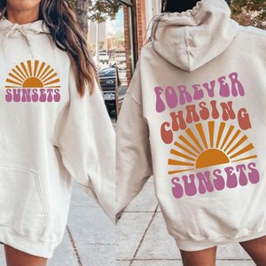May include: Two white hoodies with a graphic of a sunset and the text "FOREVER CHASING SUNSETS" and "SUNSETS".