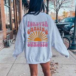 May include: Grey sweatshirt with a pink and orange graphic print that says "FOREVER CHASING SUNSETS" in a retro font.