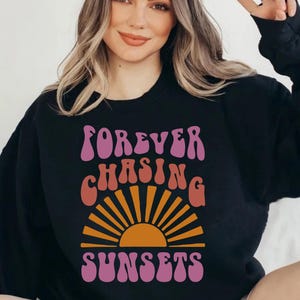 May include: Black sweatshirt with a pink, orange and yellow graphic design that says "FOREVER CHASING SUNSETS" in a retro font.