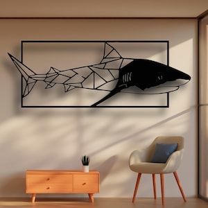 May include: Black geometric shark wall art in a rectangular frame. The shark is made of metal and has a black finish. The art is hanging on a white wall in a room with a chair and a small table.