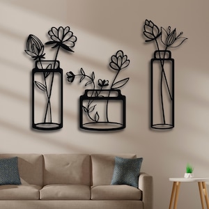 Puede incluir: Tres piezas de decoración de pared de metal negro con arreglos florales estilizados en jarrones. Los jarrones son de diferentes formas y tamaños. Las flores son dibujos lineales simples.