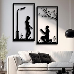 Pode incluir: Duas peças de arte de parede de metal em silhueta preta que representam um casal. A primeira peça mostra uma mulher em pé sob um poste de luz. A segunda peça mostra um homem ajoelhado com um anel na mão. Ambas as peças têm uma árvore e corações no fundo.