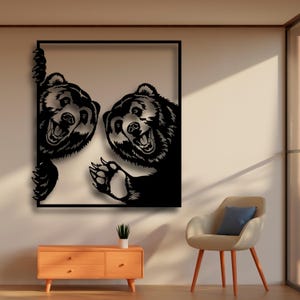Puede incluir: Arte de pared de metal negro con dos osos asomando desde un marco cuadrado. Los osos tienen una expresión juguetona con la boca abierta y los dientes visibles.