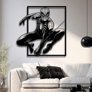May include: Black and white silhouette of Spider-Man in a web-slinging pose, framed in a black square frame. The image is mounted on a white wall.