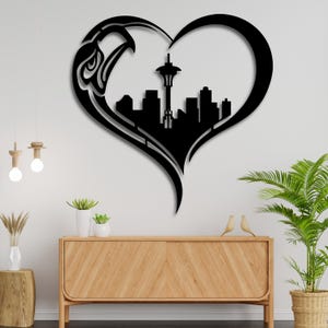 Può includere: Arte da parete in metallo nero a forma di cuore con un design di aquila stilizzato e una silhouette dello skyline di Seattle, inclusa la Space Needle.