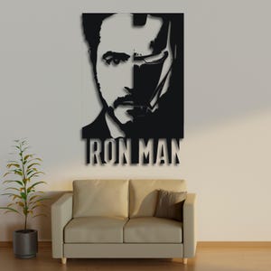 May include: Black and white silhouette of Iron Man's face with the text "IRON MAN" below. The image is displayed on a white wall above a light brown couch.
