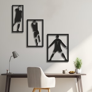 Puede incluir: Tres piezas de arte mural de metal negro que representan a jugadores de fútbol en acción. Cada pieza está enmarcada en forma rectangular. Una muestra a un jugador corriendo, otra atrapando un balón y la tercera con los brazos extendidos, con el número 7.