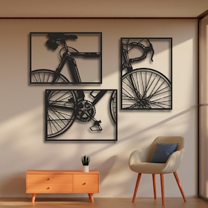 Puede incluir: Tres esculturas de pared de metal negro de bicicletas. Cada escultura es una parte diferente de una bicicleta, incluyendo el manillar, las ruedas y los engranajes.