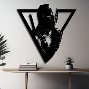 Puede incluir: Arte de pared de metal negro con una silueta de Deadpool en forma de triángulo. El personaje se muestra con el dedo en los labios, como para decir 'shhh'.