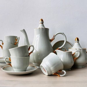 May include: A white porcelain tea set with gold accents. The set includes a teapot, creamer, sugar bowl, and four teacups and saucers.