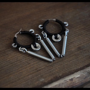 May include: A pair of black and silver earrings with a hoop design and dangling spring-like accents.