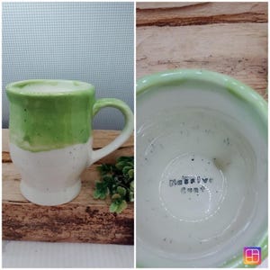 May include: A ceramic mug with a white base and a light green glazed top section. The mug features a curved handle and a speckled finish throughout. The interior bottom of the mug has the text "Massive Cunt" stamped in black ink lettering.