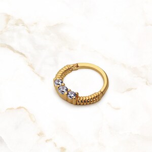 May include: Gold hoop earring with a textured band and three clear cubic zirconia stones.