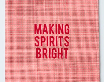 May include: A square red and white checkered napkin featuring the text "MAKING SPIRITS BRIGHT" printed in bold red capital letters in the center. The fabric has a visible woven texture throughout the entire surface of the square item.