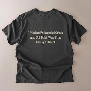 May include: Charcoal grey t-shirt featuring the phrase "I Had an Existential Crisis and All I Got Was This Lousy T-Shirt" in a plain font. The tee has a relaxed fit and a slightly worn look, suggesting a comfortable fabric.