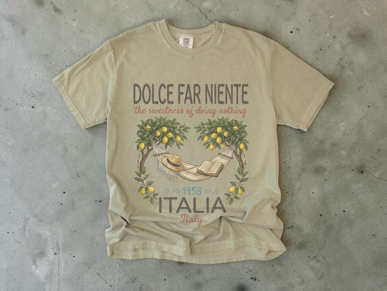 Puede incluir: Camiseta color beige con la frase "DOLCE FAR NIENTE" y "the sweetness of doing nothing". El dise&ntilde;o incluye una hamaca, un sombrero y un libro bajo limoneros, con "ITALIA" y el a&ntilde;o "1958" impresos debajo. La camiseta es de color neutro.
