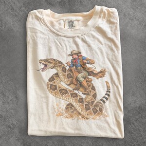 Cowboy Riding Rattlesnake Shirt, Funny Snake Tee, Unisex Comfort Colors Western Graphic T Shirt, Snake Lover Gift, Desert Rodeo Tee