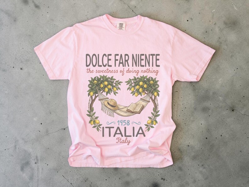 Puede incluir: Camiseta rosa claro con un dise&ntilde;o gr&aacute;fico. El dise&ntilde;o incluye una hamaca, un sombrero y un libro bajo limoneros. El texto dice "DOLCE FAR NIENTE the sweetness of doing nothing" y "1958 ITALIA Italy".