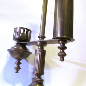 May include: A brass candlestick with three arms, each with a decorative finial. The center arm has a fluted column and a round cup at the top. The other two arms have a round cup at the top and a cylindrical tube.