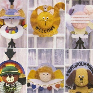 May include: A craft pattern featuring six different door hangers. The hangers are made from straw hats and feature a variety of animal and holiday themes. The themes include a bunny, a cat, an angel, a bear, a dog, and a girl. The pattern includes instructions for making each hanger.