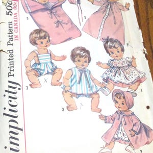 May include: Vintage Simplicity printed pattern featuring illustrations of baby dolls in various outfits. The pattern includes a baby in a pink sleeping bag, a pink robe, and other clothing options. The pattern is marked "Printed Pattern 50c IN CANADA 60c".