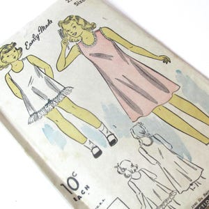 May include: Vintage sewing pattern for a simple slip dress with a lace trim. The pattern is for a child's dress and includes instructions for cutting and sewing. The pattern is printed on paper and is in black and white.