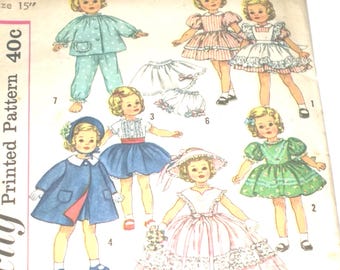 May include: Vintage doll clothing pattern featuring illustrations of various outfits, including a blue coat, a pink dress, and a green dress. The pattern is for a 15-inch doll and includes a pajama set. The price is 40 cents.
