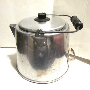 May include: A silver aluminum camping coffee pot with a black handle and a lid. The pot has a wire handle with a black wooden grip.