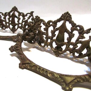 May include: Two antique bronze drawer pulls with ornate, filigree designs. The pulls feature a curved handle and a decorative, openwork pattern with floral and scroll motifs. The metal has a weathered, aged appearance, suggesting vintage craftsmanship.