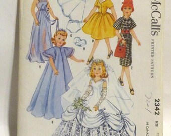 May include: Vintage McCall's sewing pattern for a doll's wardrobe. The pattern includes five different outfits: a long blue dress, a short yellow dress, a white dress with a lace overlay, a blue dress with a cape, and a red and white gingham dress. The pattern is for dolls with high heels and is designed for Revlan, Toni Sophisticate, Cindy, Missy, Junior Miss, Little Lady and Sweet Sue Sophisticate Dolls. The pattern number is 2342.